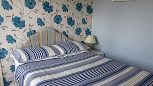 Een net opgemaakt bed met gestreept beddengoed, een bedlampje en bloemenbehang.