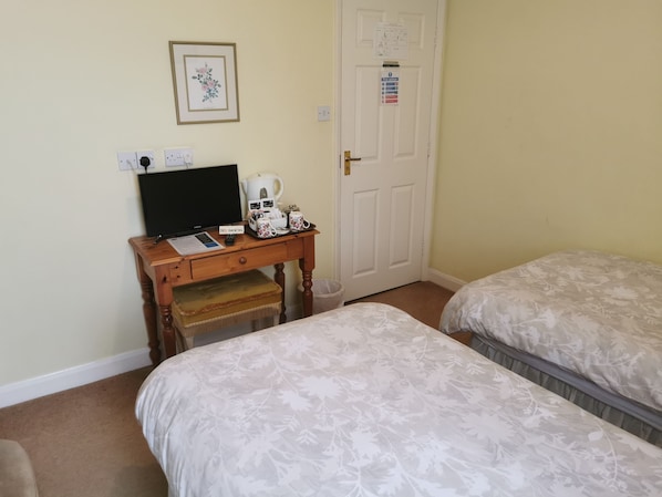 A hotel room with two beds, a desk with a laptop, a television, and a small table with a teapot and cups. - Black Swan Guest House (Gainsborough)