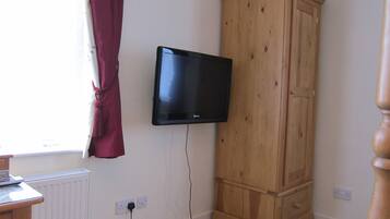A room with a wooden wardrobe, a mounted television, a radiator, and a window with curtains.