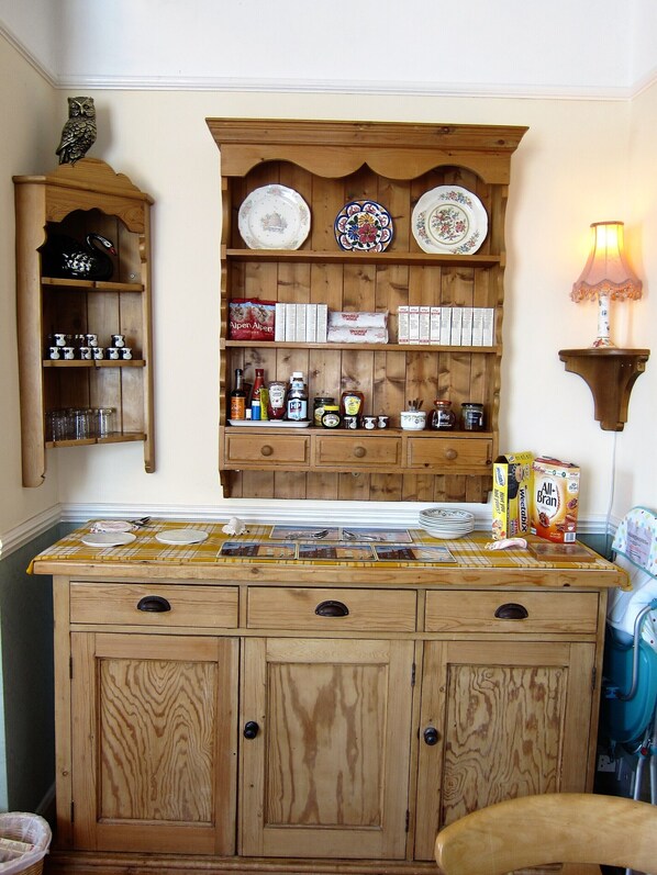 A kitchen with wooden cabinets, a central island, and a hanging shelf with plates and jars. - Black Swan Guest House (Gainsborough)