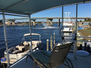 Una terraza cubierta con asientos, vistas de un río con un puente, y un muelle con barcos.