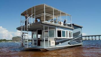 A houseboat with a covered deck, a balcony, and a view of a pier in the background.