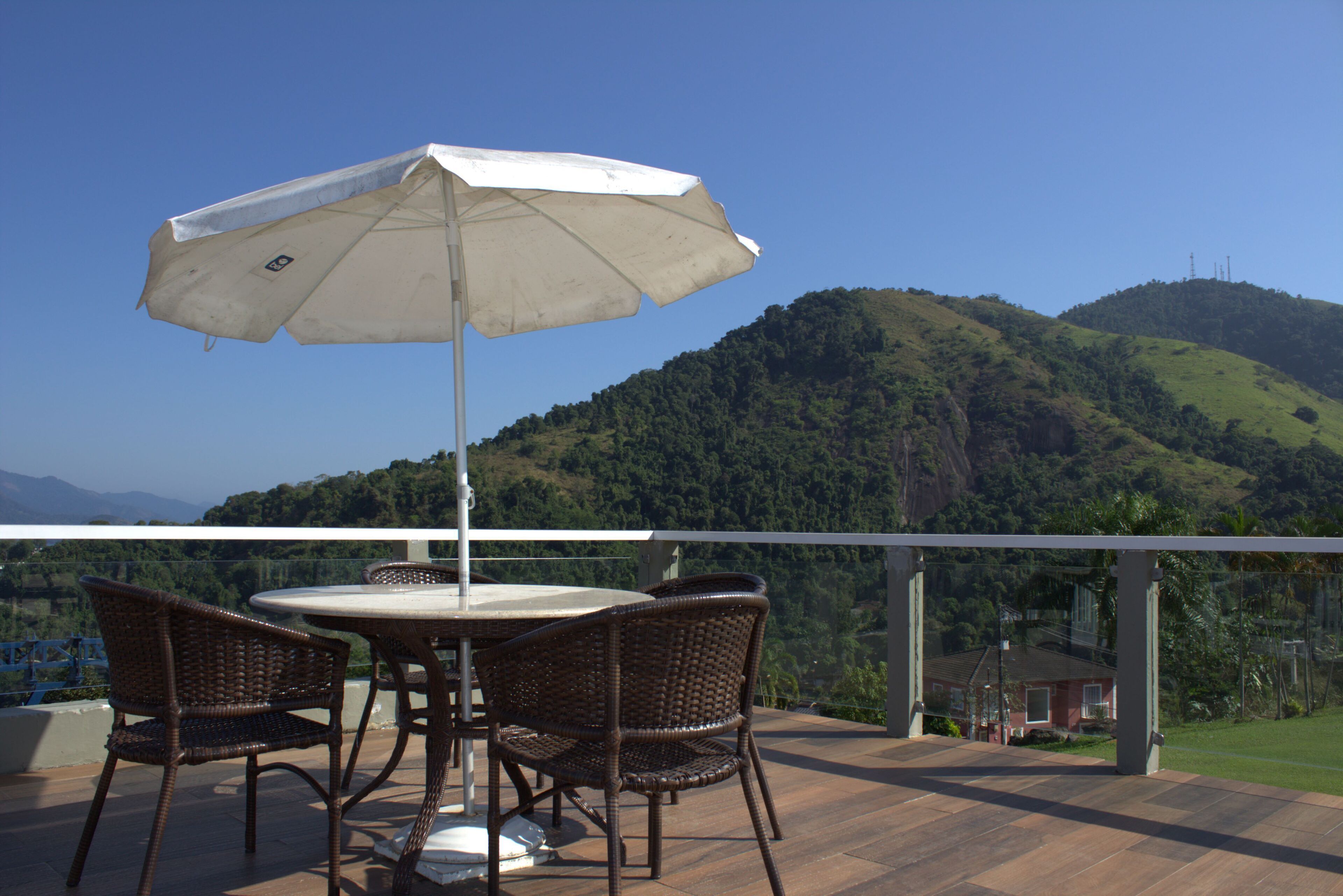 Une terrasse extérieure avec des chaises en osier et une table placée sous un parasol blanc, offrant une vue sur un paysage montagneux.