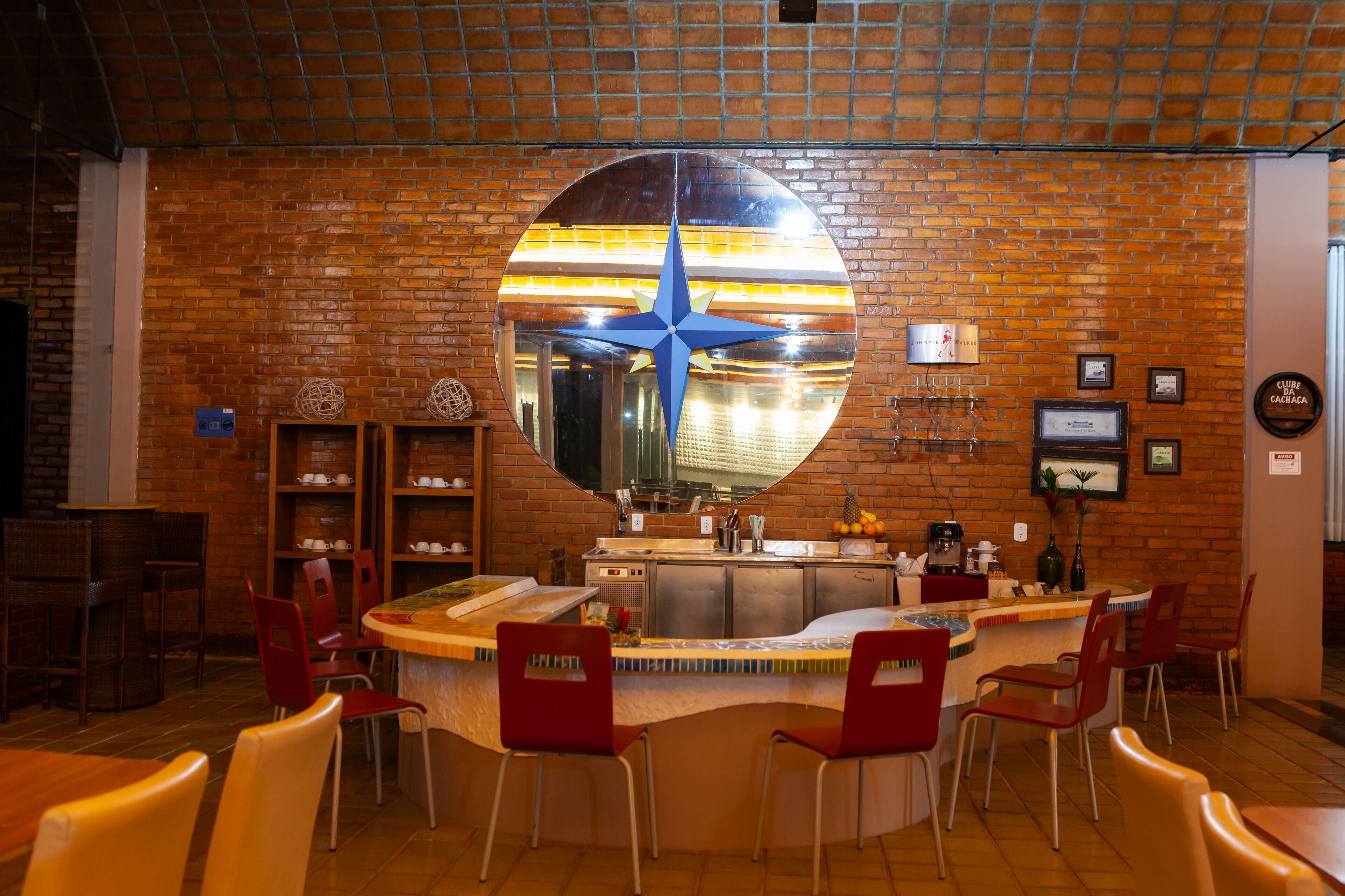 Un restaurant avec un mur en briques, un grand miroir rond et des chaises rouges.
