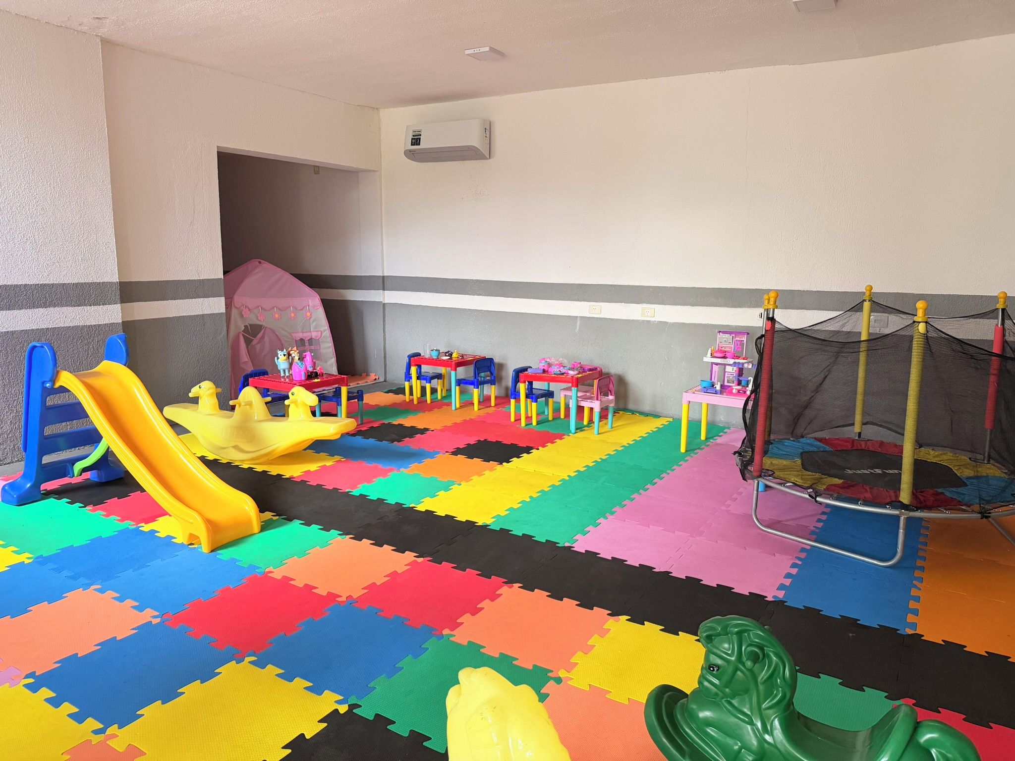 A children's play area with a slide, tables, chairs, and a trampoline.