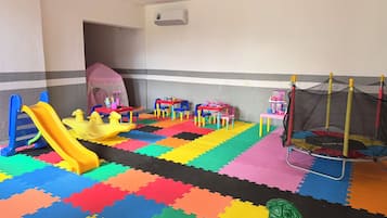 A children's play area with a slide, tables, chairs, and a trampoline.