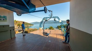 A wooden deck with a cable car system, a sign indicating a maintenance area, and a view of the sea and hills.