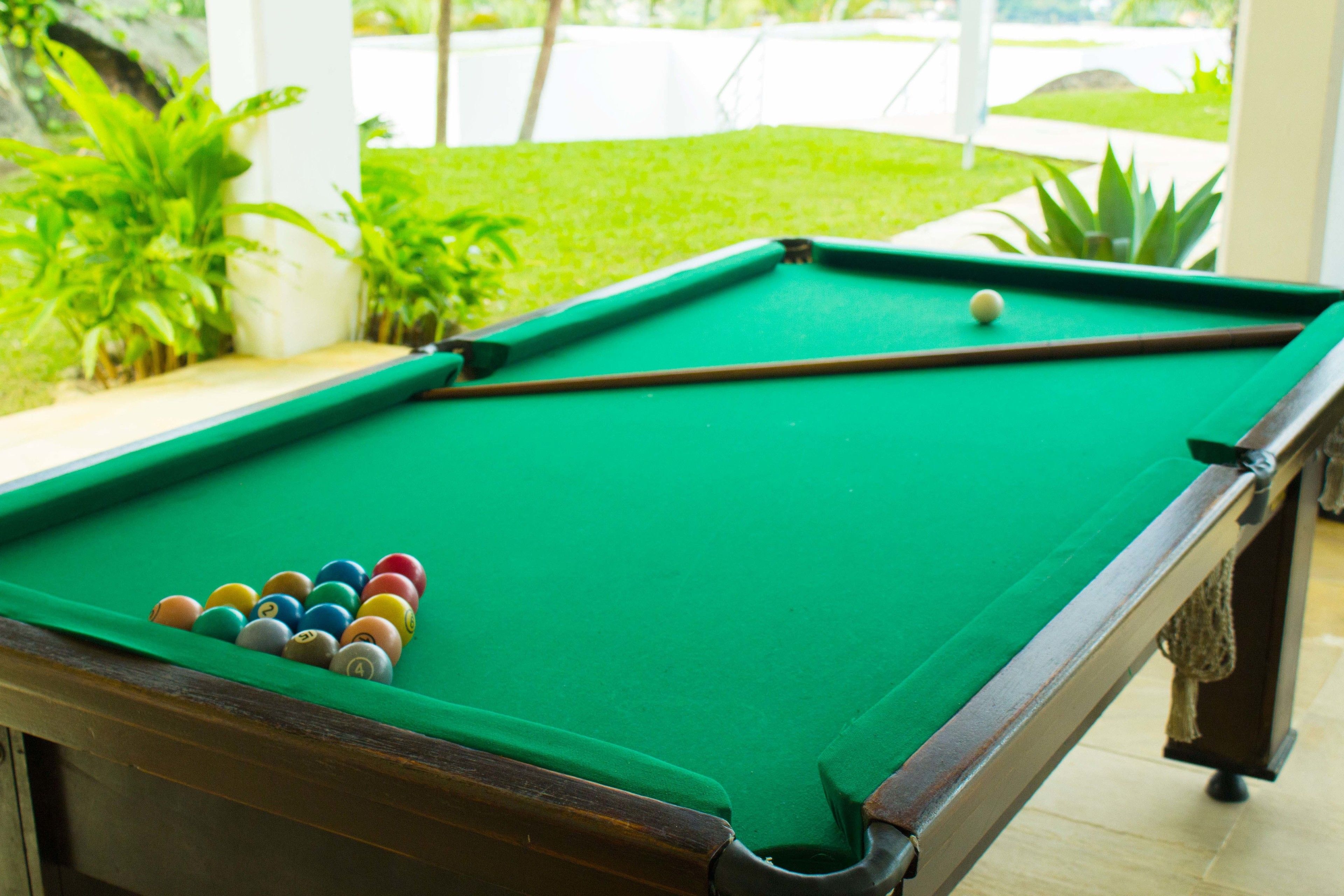 A pool table with balls in a room with a view of a garden.