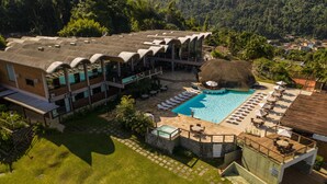 A resort with a swimming pool, outdoor seating, and a thatched-roof structure. - Portogalo Suite Hotel (Angra dos Reis)