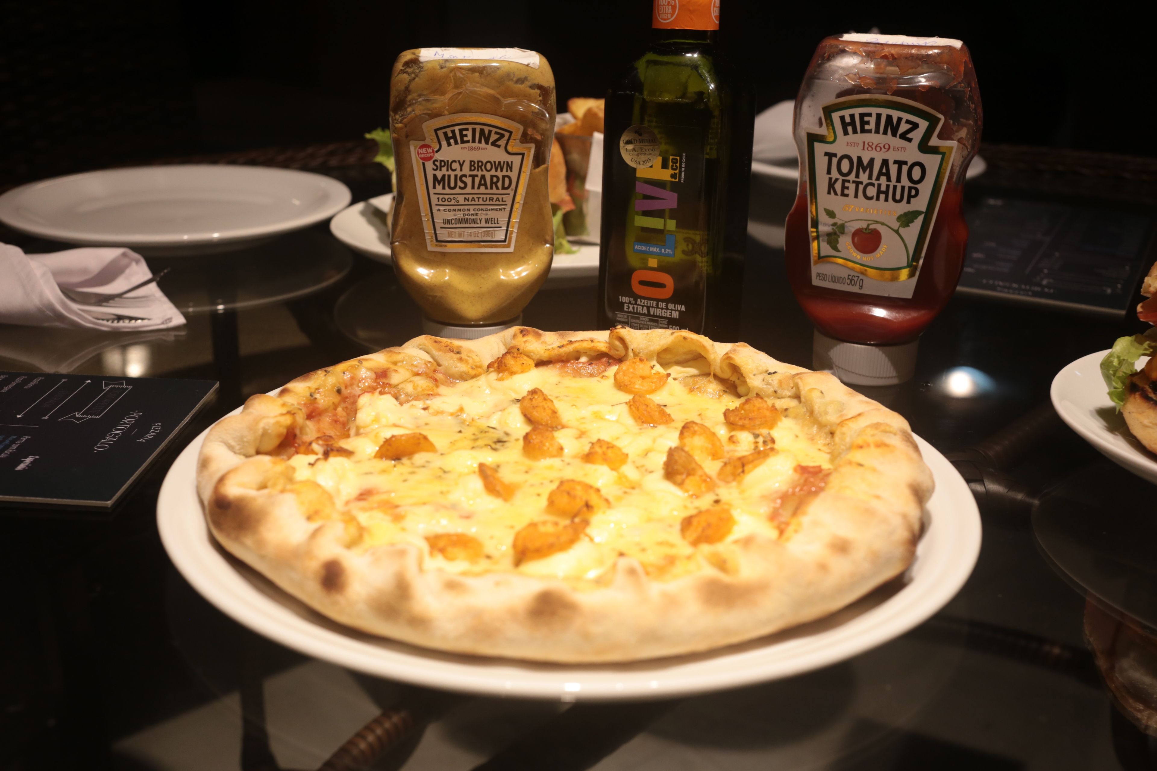 A pizza on a plate with condiments including Heinz Tomato Ketchup and Heinz Spicy Brown Mustard.