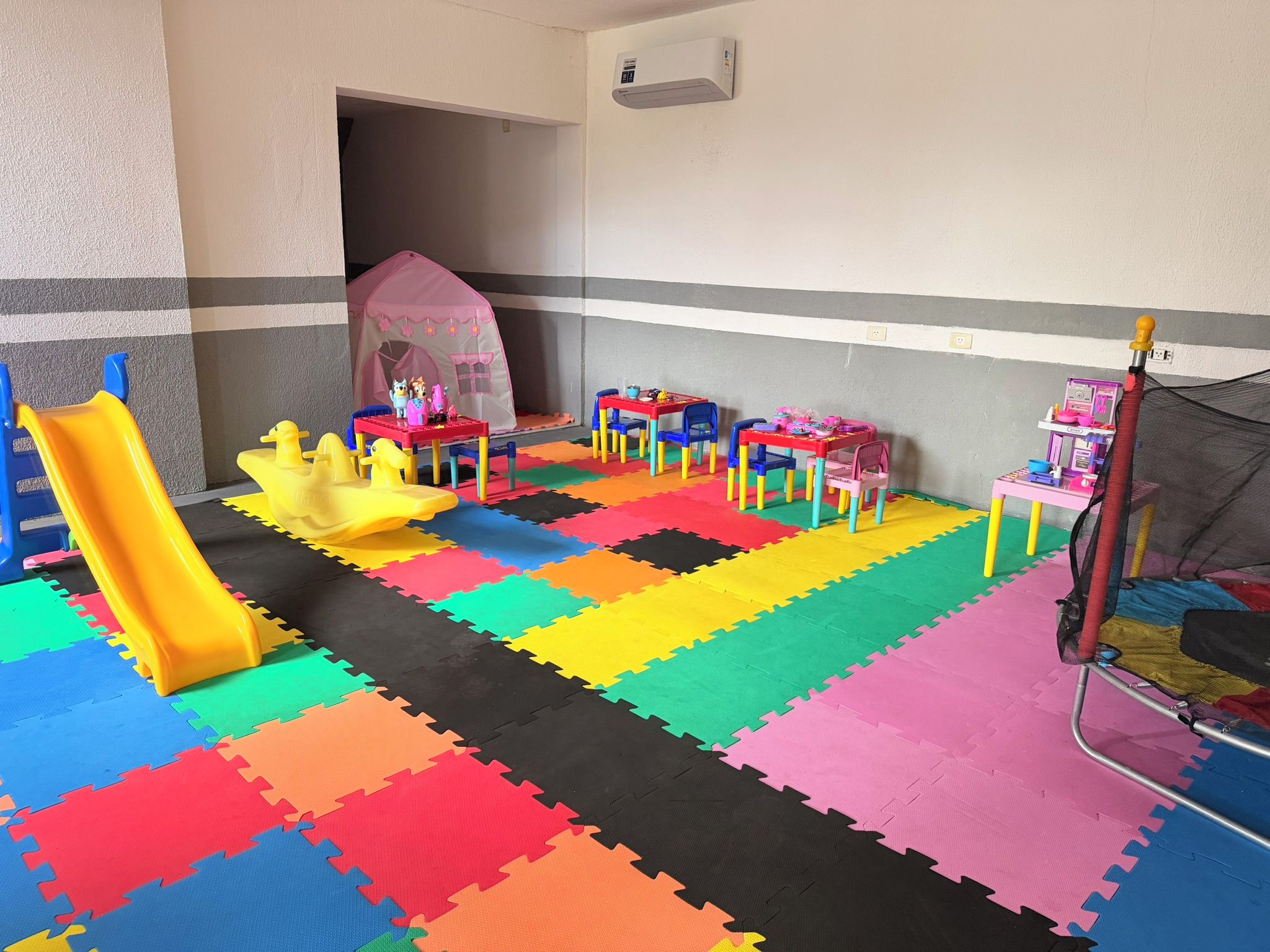Ein Spielzimmer mit Rutsche, Spieltischen und einem Zelt.