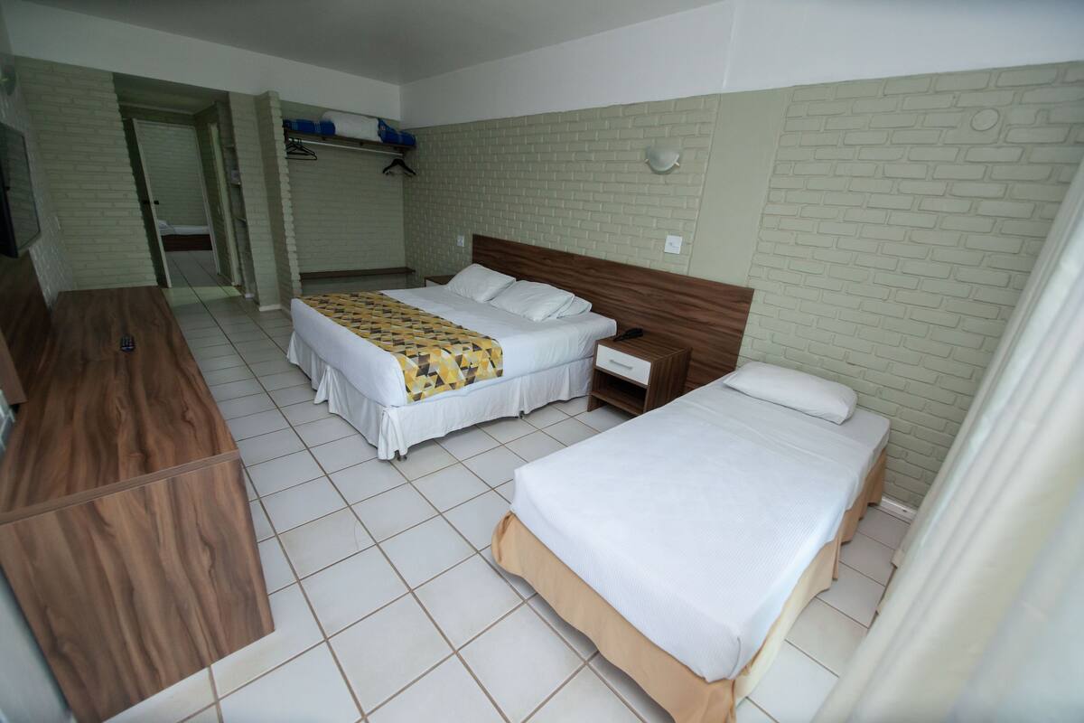 A hotel room with two beds, a wooden desk, a wardrobe, and a bathroom visible through an open door.