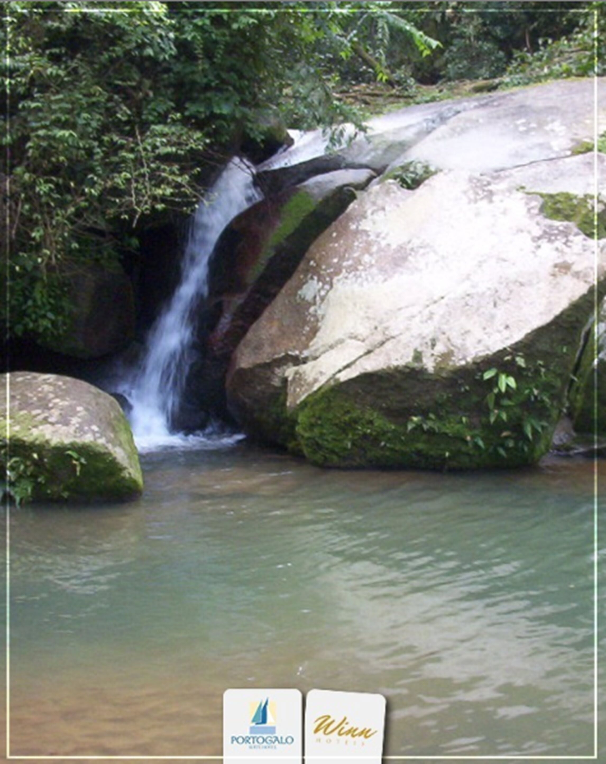 Uma cascata natural cercada por pedras grandes e vegetação.