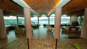 A spacious lobby with a tiled floor, large windows offering a view of the sea, and a central staircase. - Portogalo Suite Hotel (Angra dos Reis)