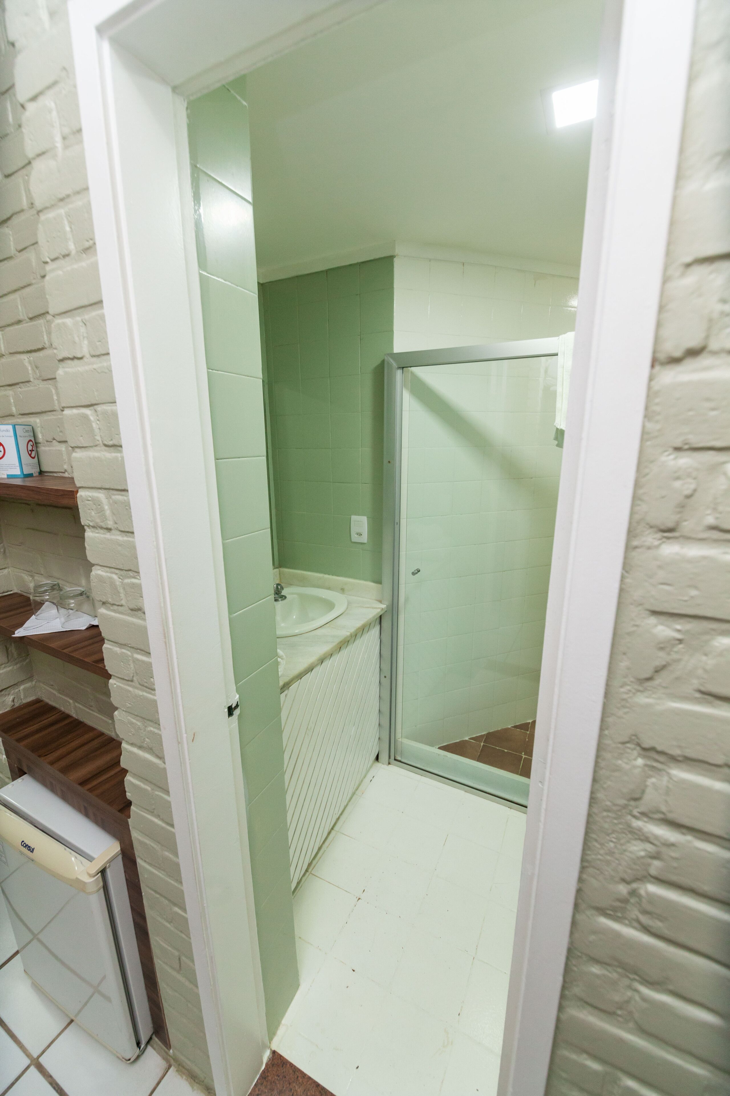 A bathroom with a white sink, a glass shower enclosure, and a brick wall.