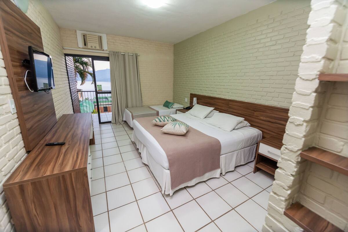 A hotel room with a bed, a desk, a TV, and a balcony with a view.