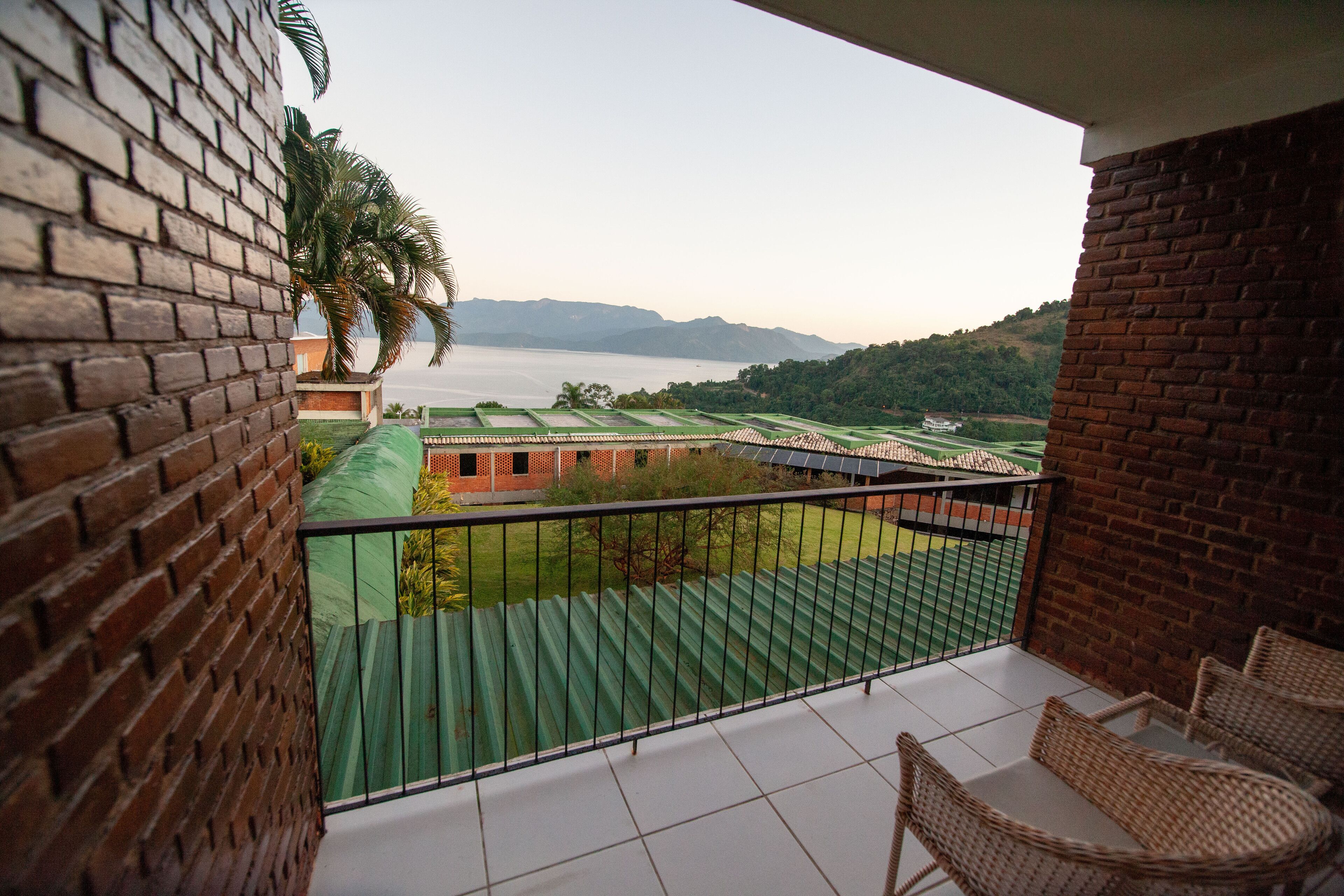 A balcony with wicker chairs, a view of a green field, and a distant body of water.
