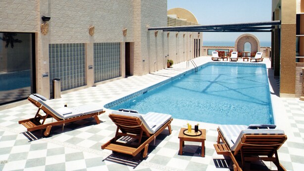 A rooftop pool with lounge chairs and a view of the ocean. - Elite Tower (Manama)