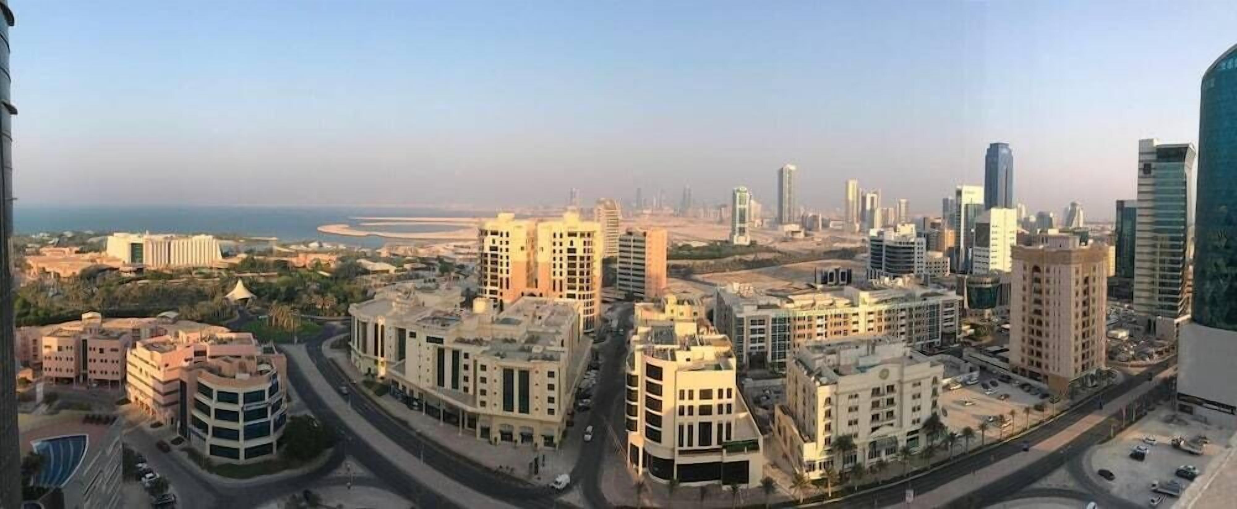A cityscape with modern buildings, roads, and a distant view of the sea.