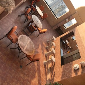 A dining area with round tables and orange chairs, a tiled floor, and a view of buildings through a large window.
