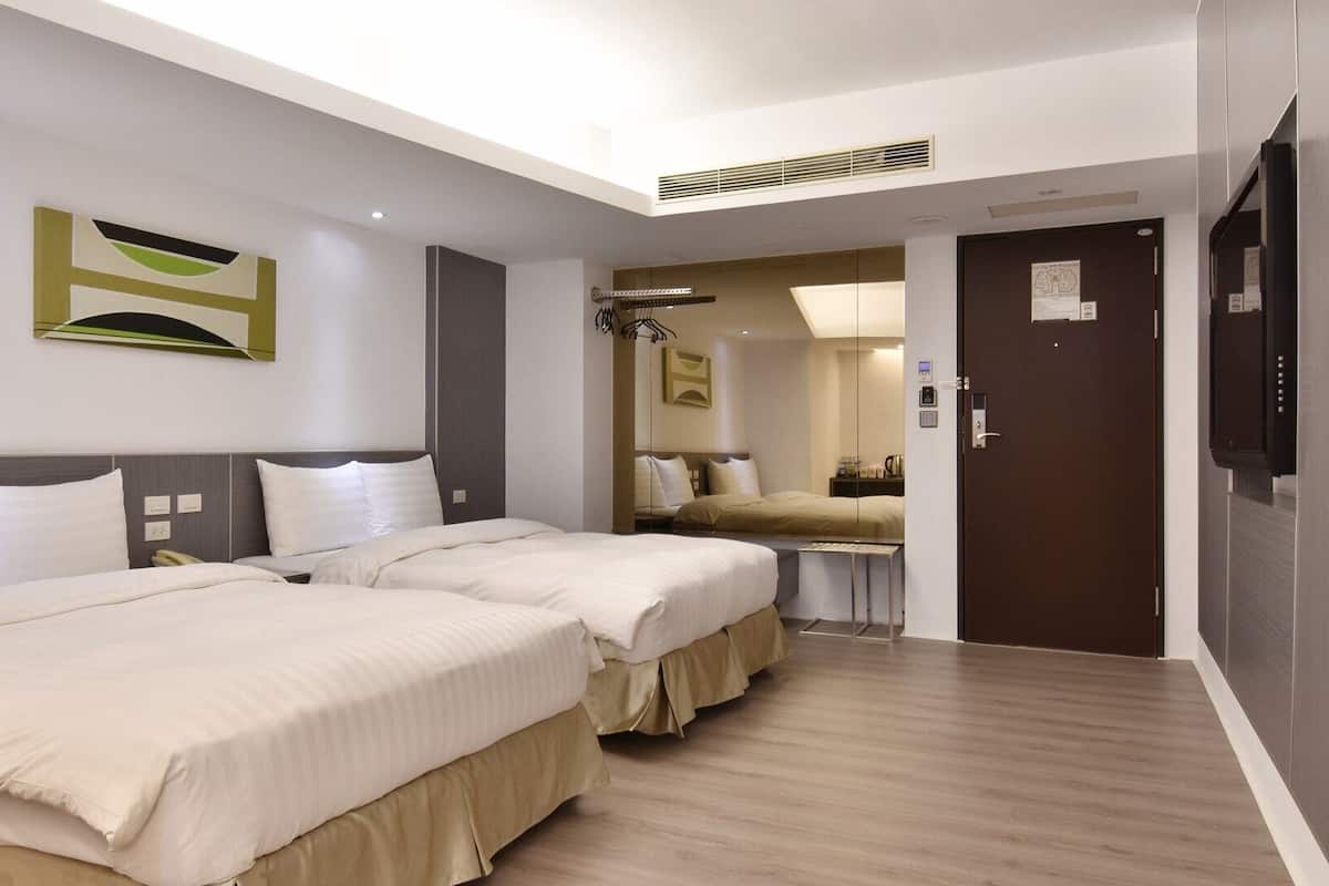Habitación de hotel con dos camas, una mesita, un espejo y una puerta.