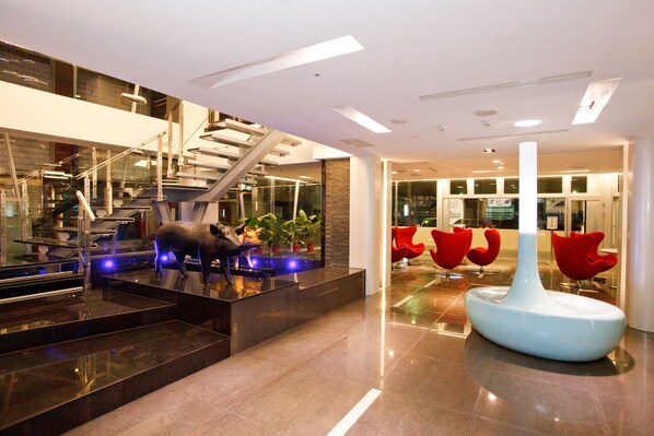 A modern lobby with a staircase, a reception desk, and red chairs.