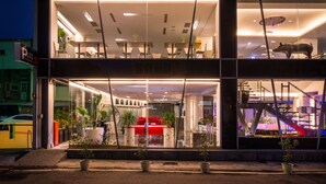 A modern building with large glass windows, a red interior, and multiple potted plants on the ground level. - Hotel Hi Xinmin (Chiayi City)