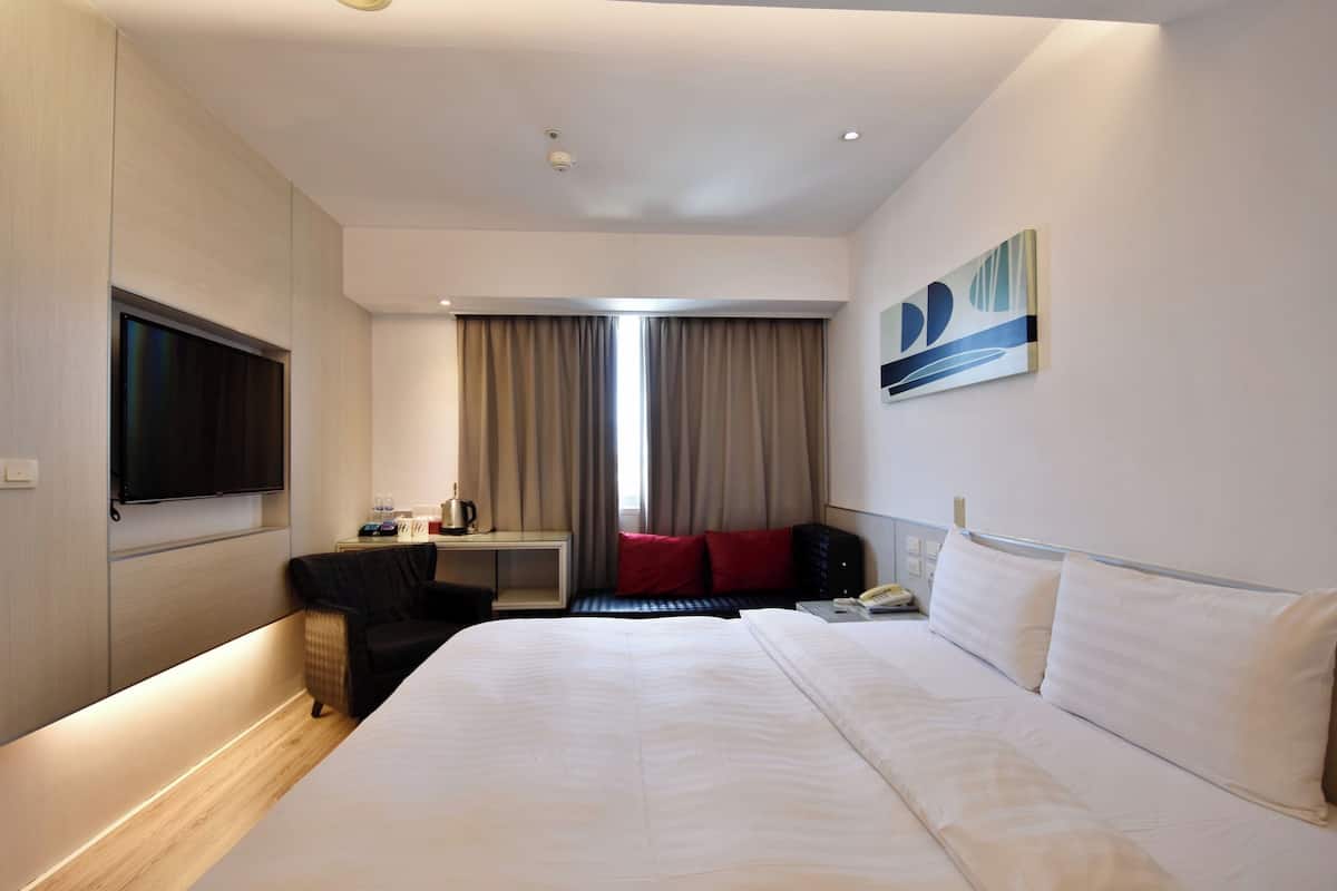 Habitación de hotel con una cama grande, un televisor de pantalla plana montado en la pared, un escritorio con una silla, una ventana con cortinas y un cuadro en la pared.