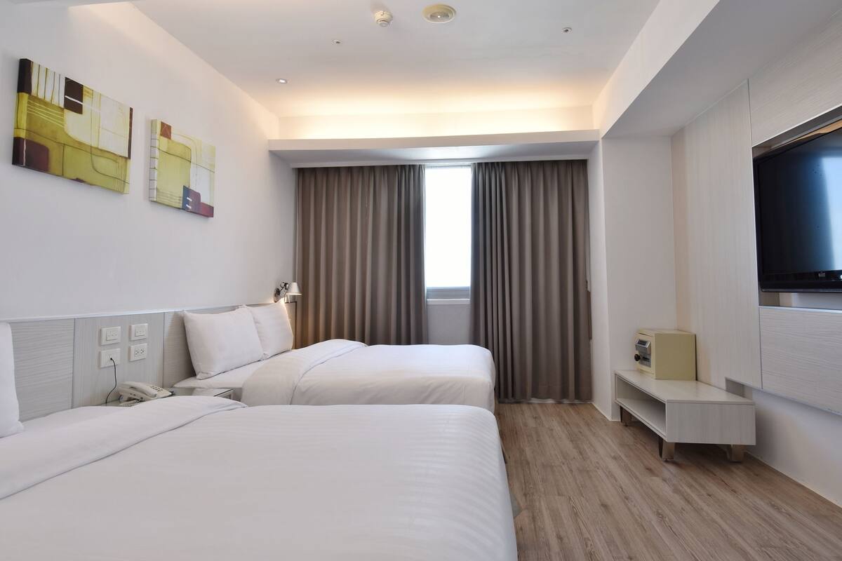 Una habitación de hotel con dos camas, televisión, escritorio y ventana con cortinas.