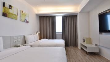 Quarto de hotel com duas camas, televisão, secretária e janela com cortinas.