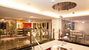 A modern hotel lobby with a glass staircase, a reception desk, and a dining area with chairs and tables. - Hotel Hi Xinmin (Chiayi City)