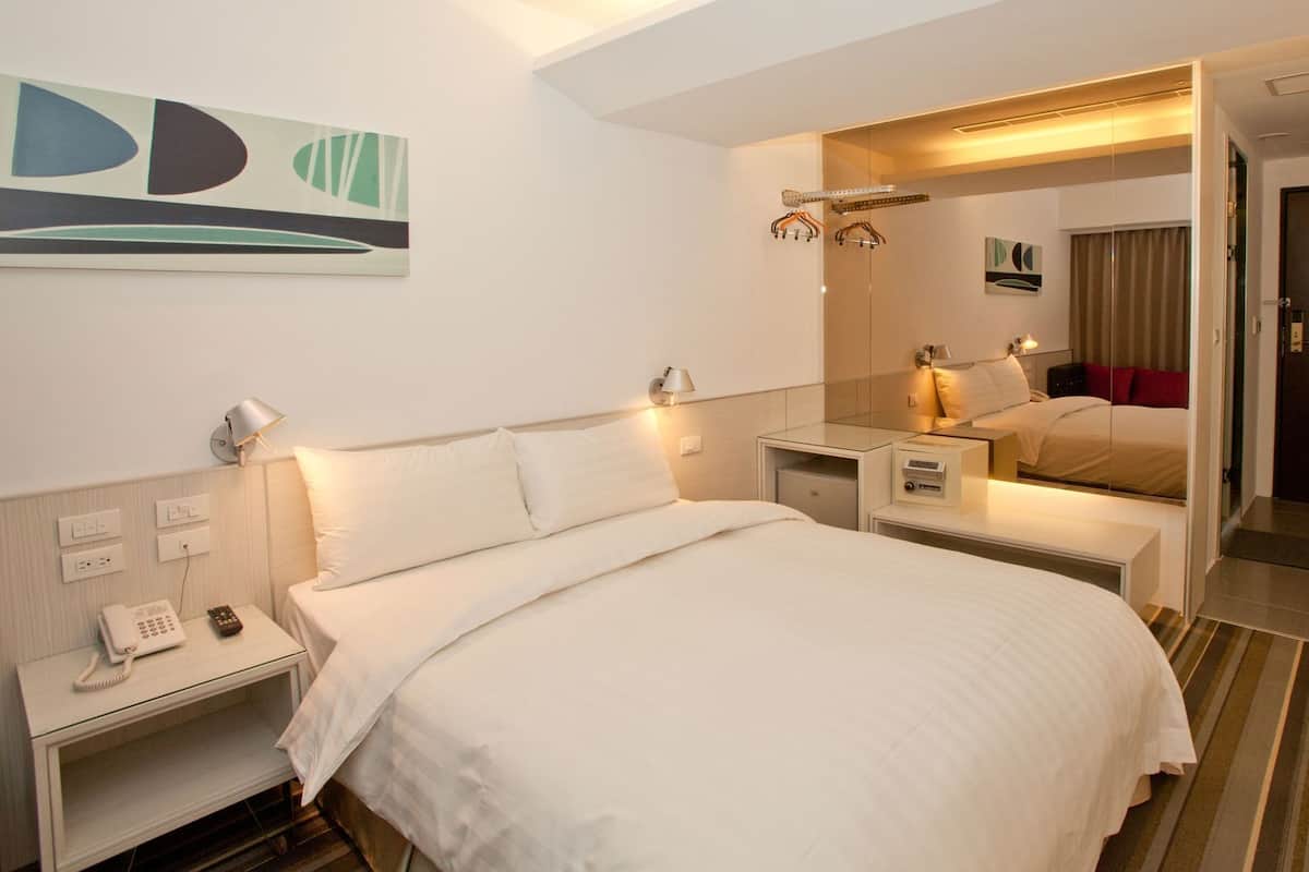 Habitación de hotel con cama, mesitas de noche, teléfono, lámpara, espejo y un cuadro en la pared.