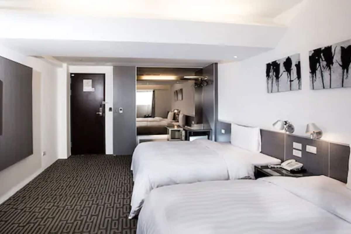 Habitación de hotel con dos camas, un escritorio, una silla, un espejo y obras de arte en la pared.