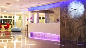 A modern hotel lobby with a reception desk, a large wall clock, and a marble column. - Hotel Hi Xinmin (Chiayi City)
