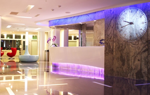 A modern hotel lobby with a reception desk, a large wall clock, and a marble column. - Hotel Hi Xinmin (Chiayi City)