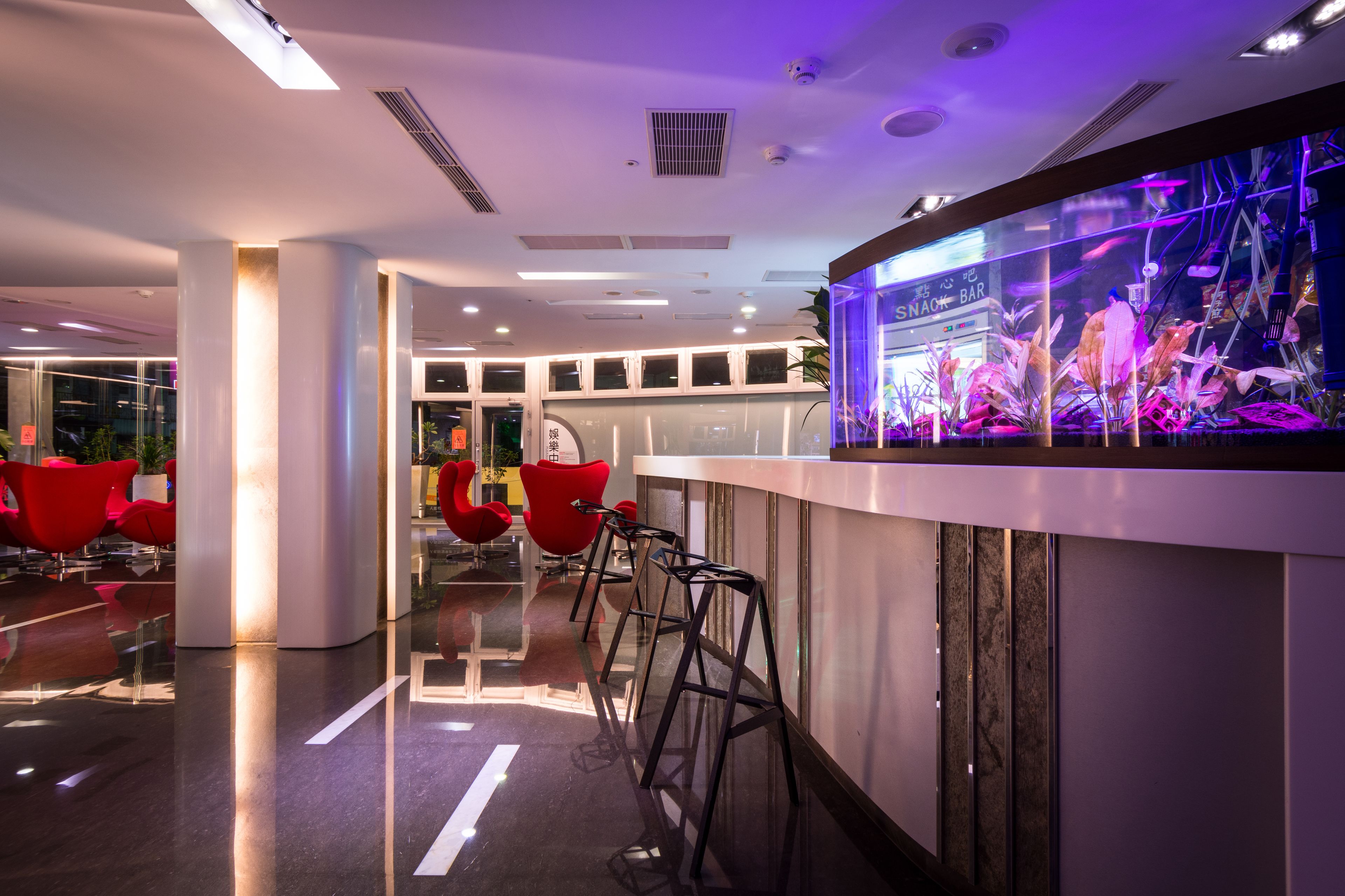 Zona de bar moderna con un acuario grande, sillas rojas y piso pulido.