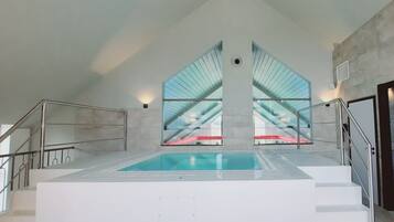 Une piscine au design moderne, entourée d’un intérieur blanc et dotée d’un plafond haut.