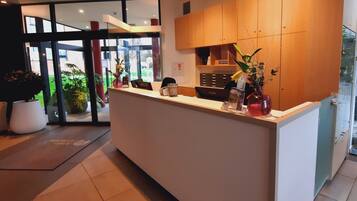 A reception area with a white reception desk, wooden cabinets, and potted plants.