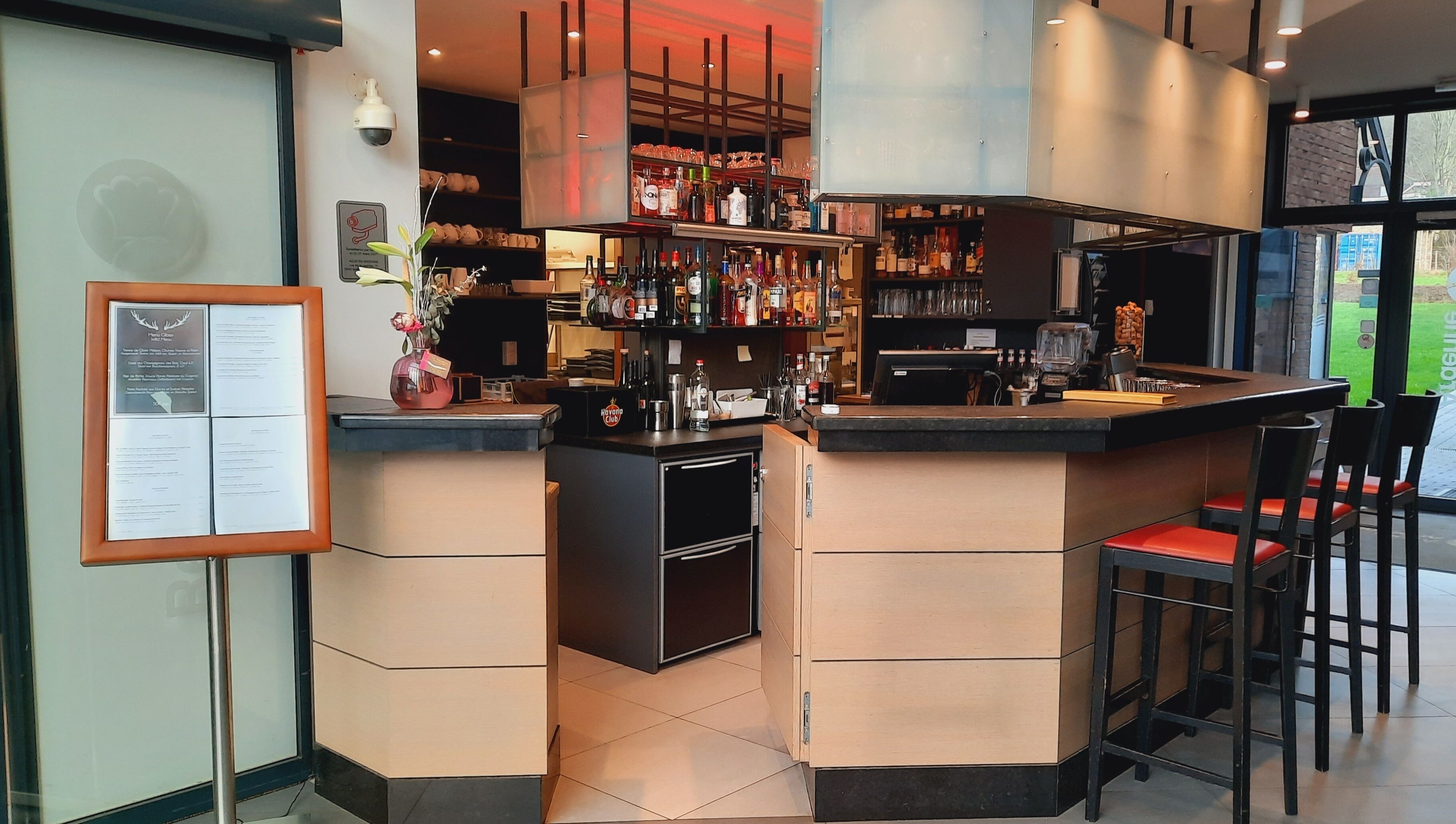 Una zona de bar con mostrador, taburetes y estantes llenos de botellas.