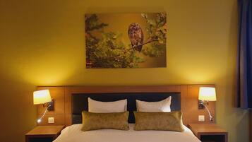 Een hotelkamer met een groot bed, twee bedlampjes, een hoofdeinde en een aan de muur hangend schilderij van een uil.