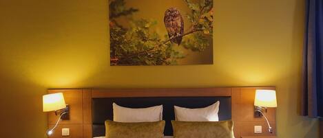 Una habitación de hotel con una cama grande, dos lámparas de noche, un cabecero y un cuadro de un búho colgado en la pared.