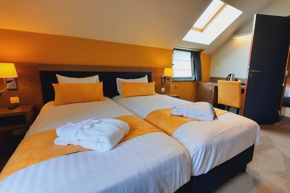 Ein Hotelzimmer mit zwei Betten, einem Oberlicht, einem Schreibtisch und einem Badezimmer.