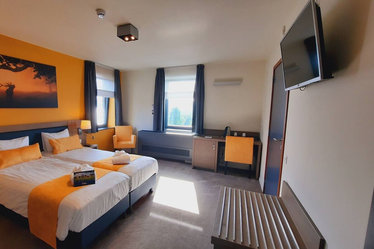 Ein Hotelzimmer mit einem großen Bett, einem Schreibtisch, einem Sessel, einem Fernseher und einem Gemälde an der Wand.