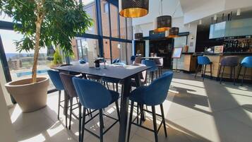 A modern dining area with a large table and blue chairs, a potted tree, and a bar with stools.