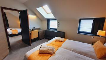 A hotel room with a bed, a desk, a chair, a mirror, a window, and a skylight.