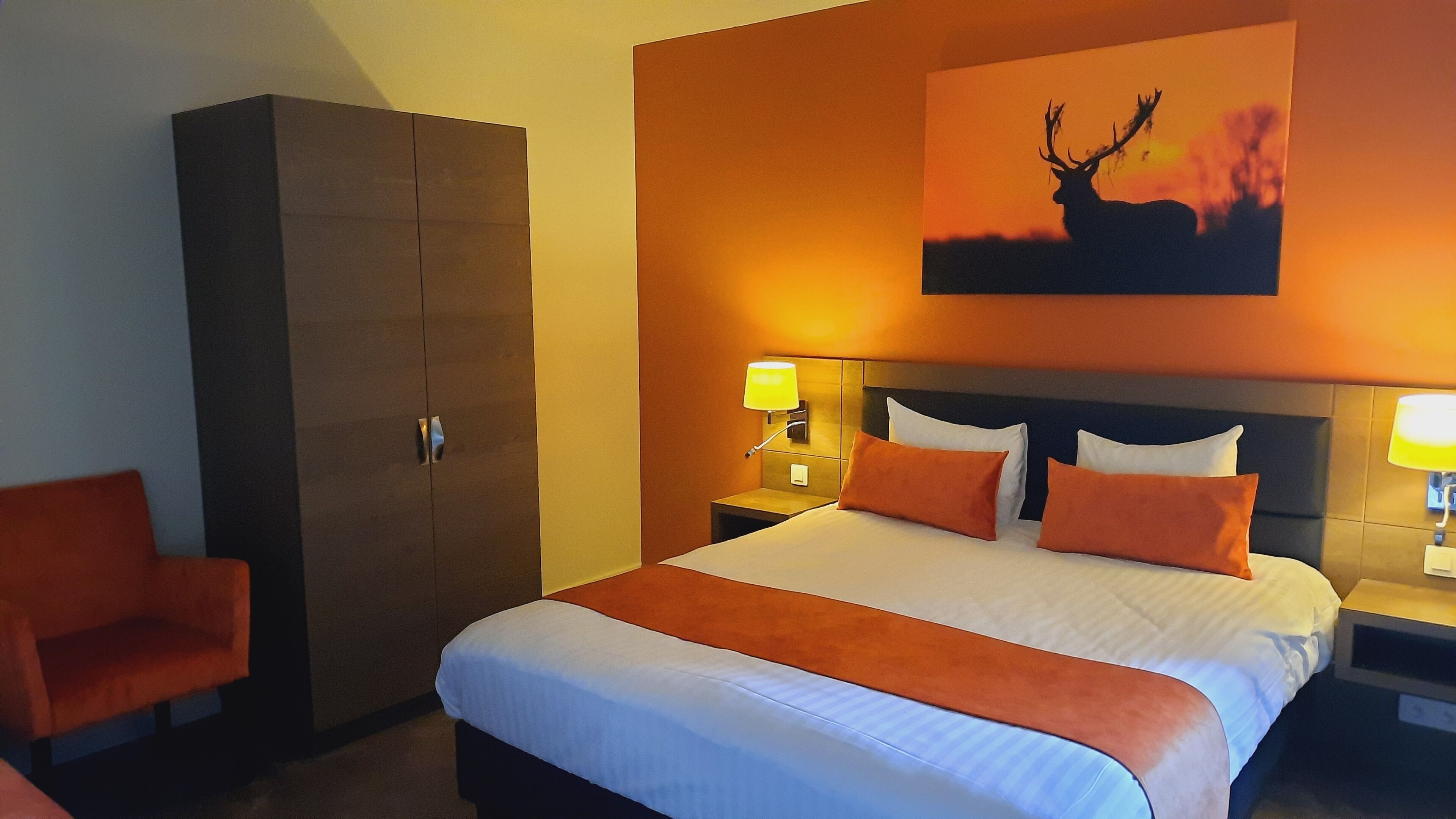A hotel room with a large bed, two nightstands, a wardrobe, and a painting of a deer on the wall.