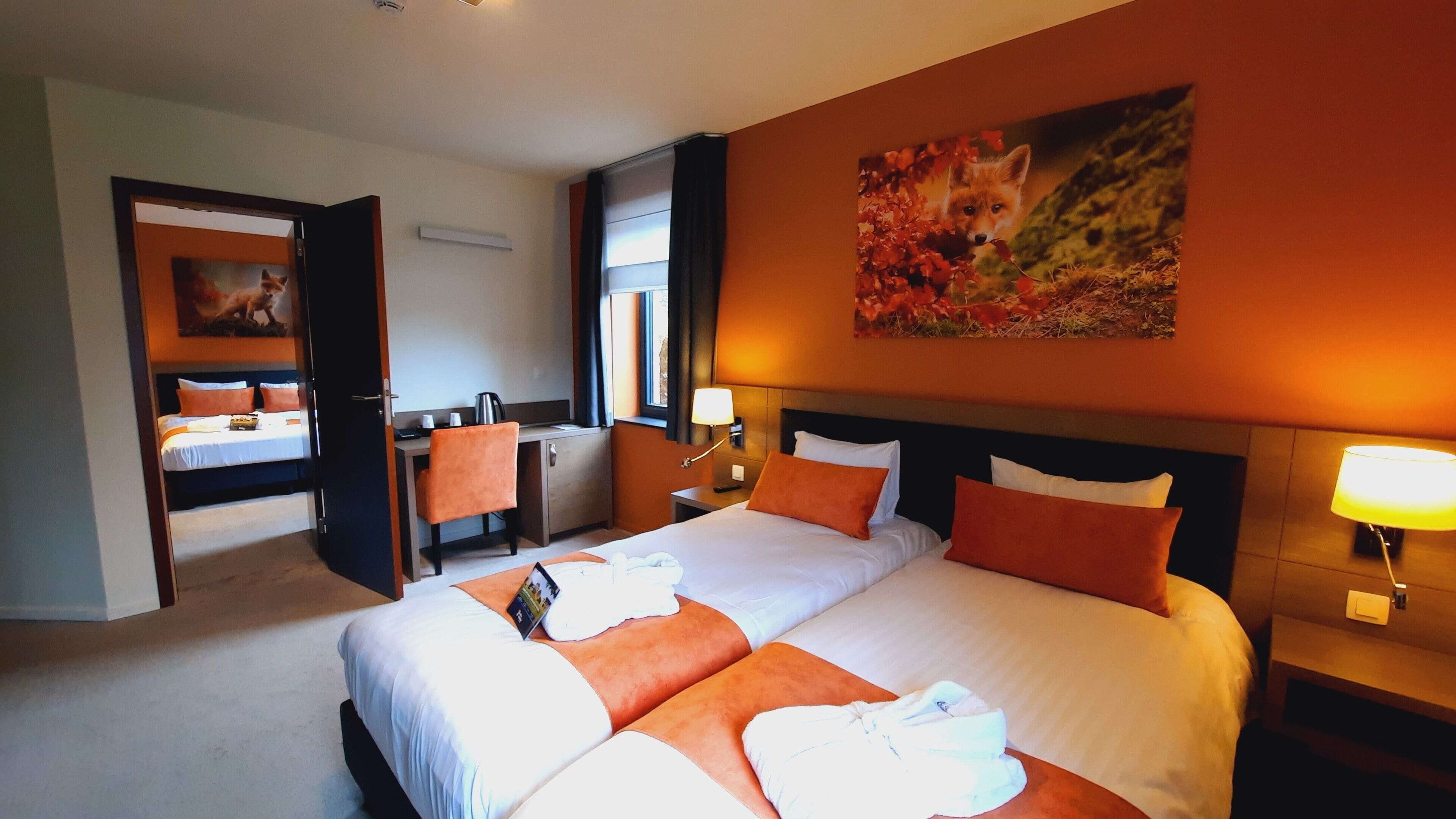 Ett hotellrum med en stor säng, ett skrivbord och en stol. Det finns en tavla på väggen och ett fönster med gardiner.