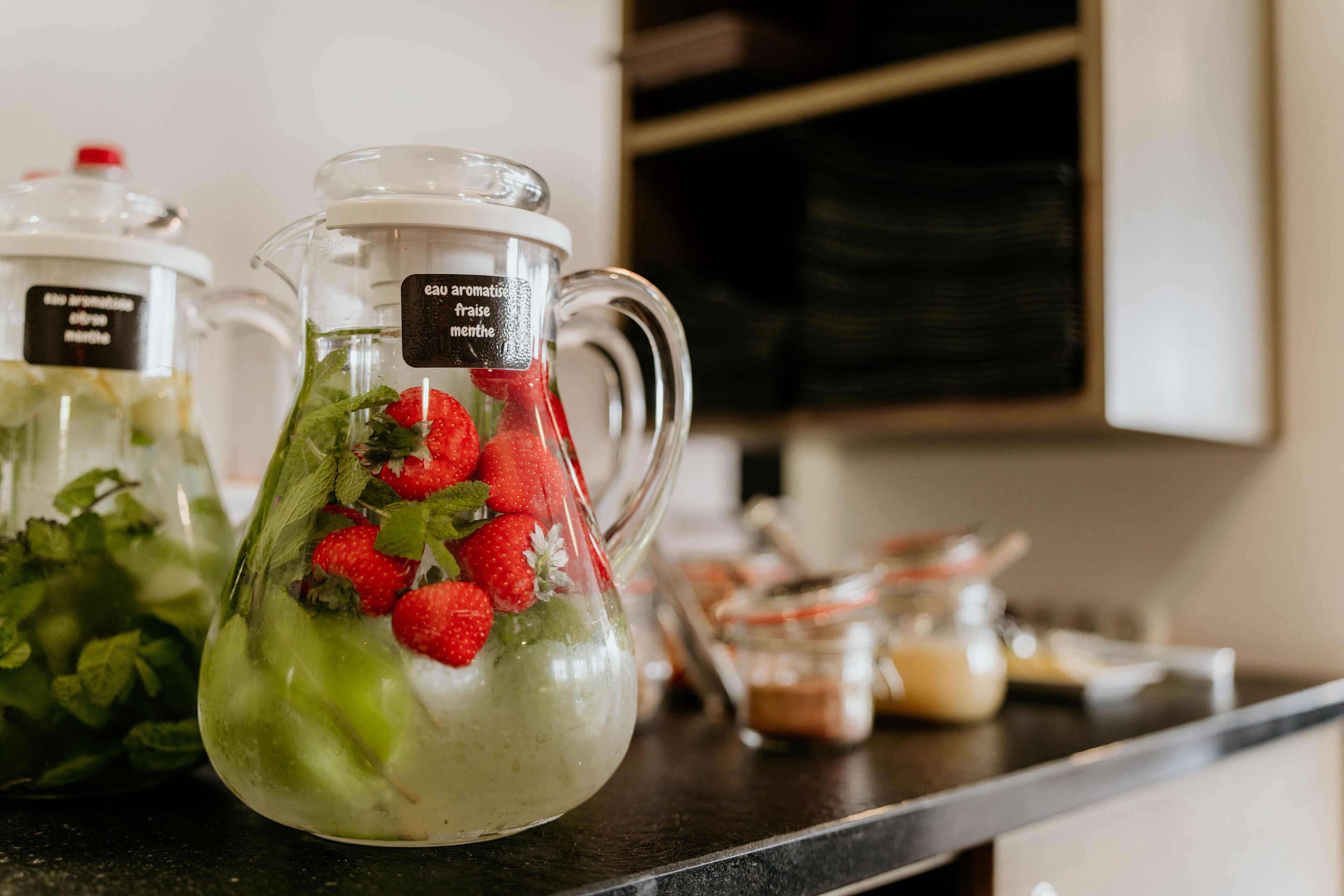 A kitchen counter with a pitcher containing a green beverage garnished with strawberries and mint leaves.