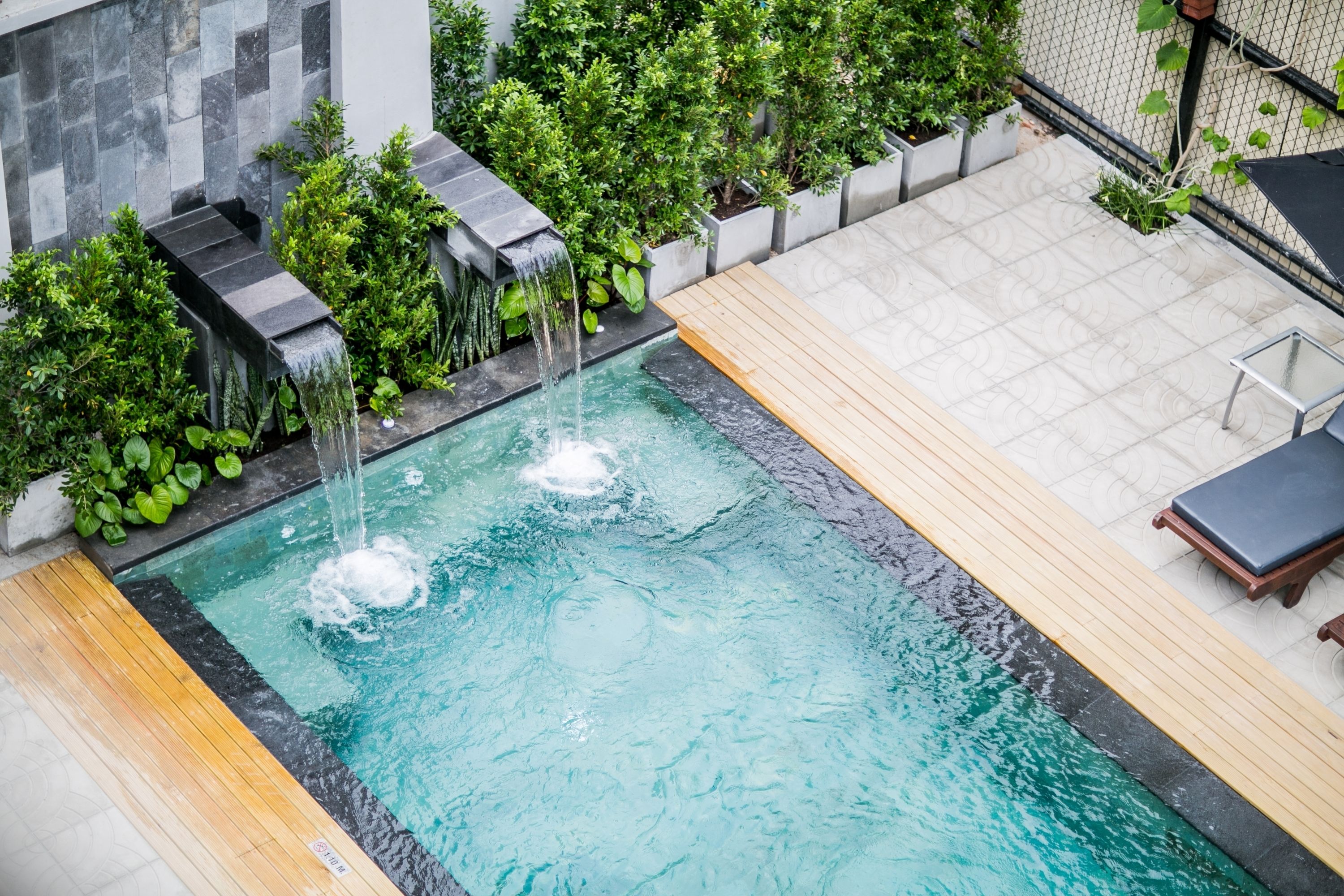 Ein Pool auf dem Dach mit einer Holzterrasse, umgeben von Grünpflanzen und einer Steinmauer.