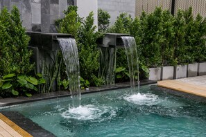 Una piscina con dos cascadas, rodeada de abundante vegetación y un muro de piedra.